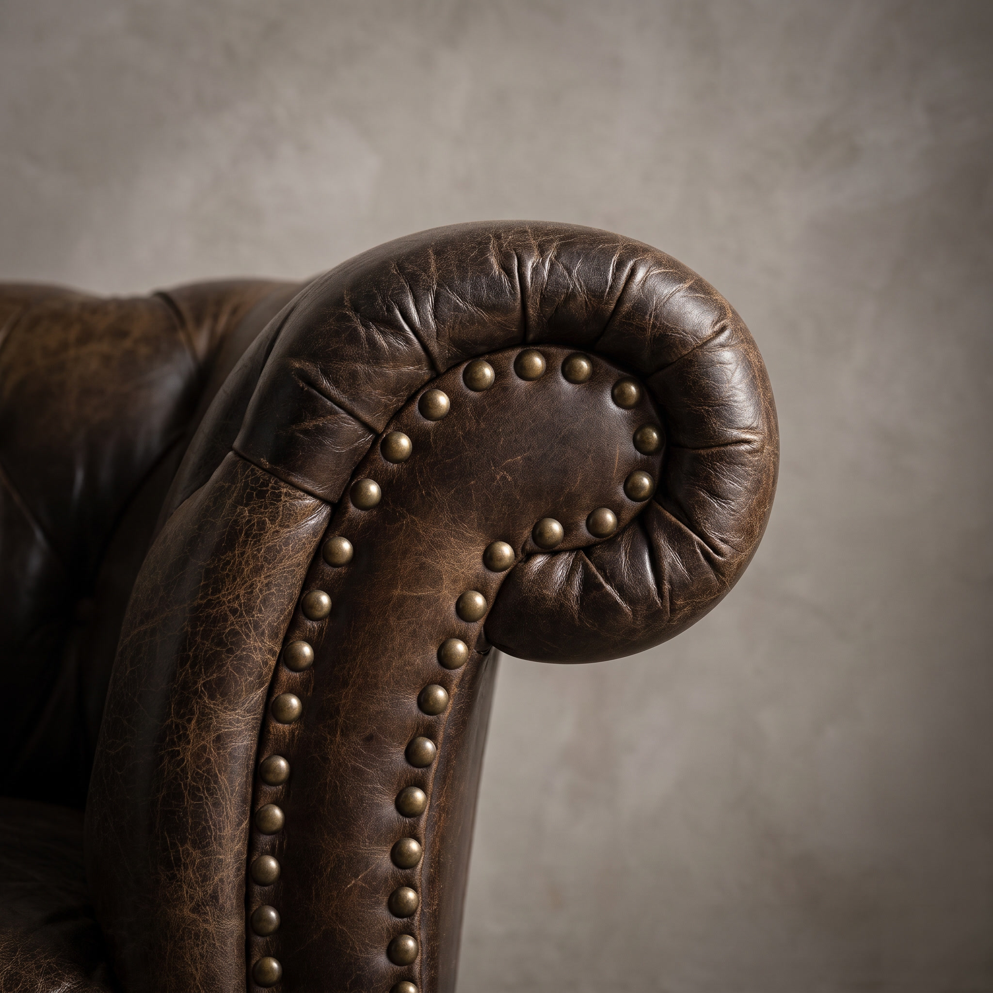 Macro detail of the arm scroll and aged brass nailhead trim on The Umber Chesterfield, matte worn leather