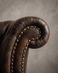 Macro detail of the arm scroll and aged brass nailhead trim on The Umber Chesterfield, matte worn leather