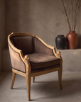 Carved whitewashed bergere chair, brown suede, against raw plaster wall