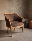 Carved whitewashed bergere chair, brown suede, against raw plaster wall