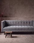 Blue-grey velvet biscuit-tufted sofa against raw plaster wall