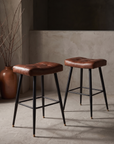 Pleather saddle counter stools, pair, against raw plaster wall