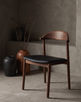 Count On Me walnut dining chair with black seat against raw plaster wall