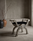 Bone inlay curule bench, three-quarter view, in a greige plaster room with stoneware vessels and dried branches