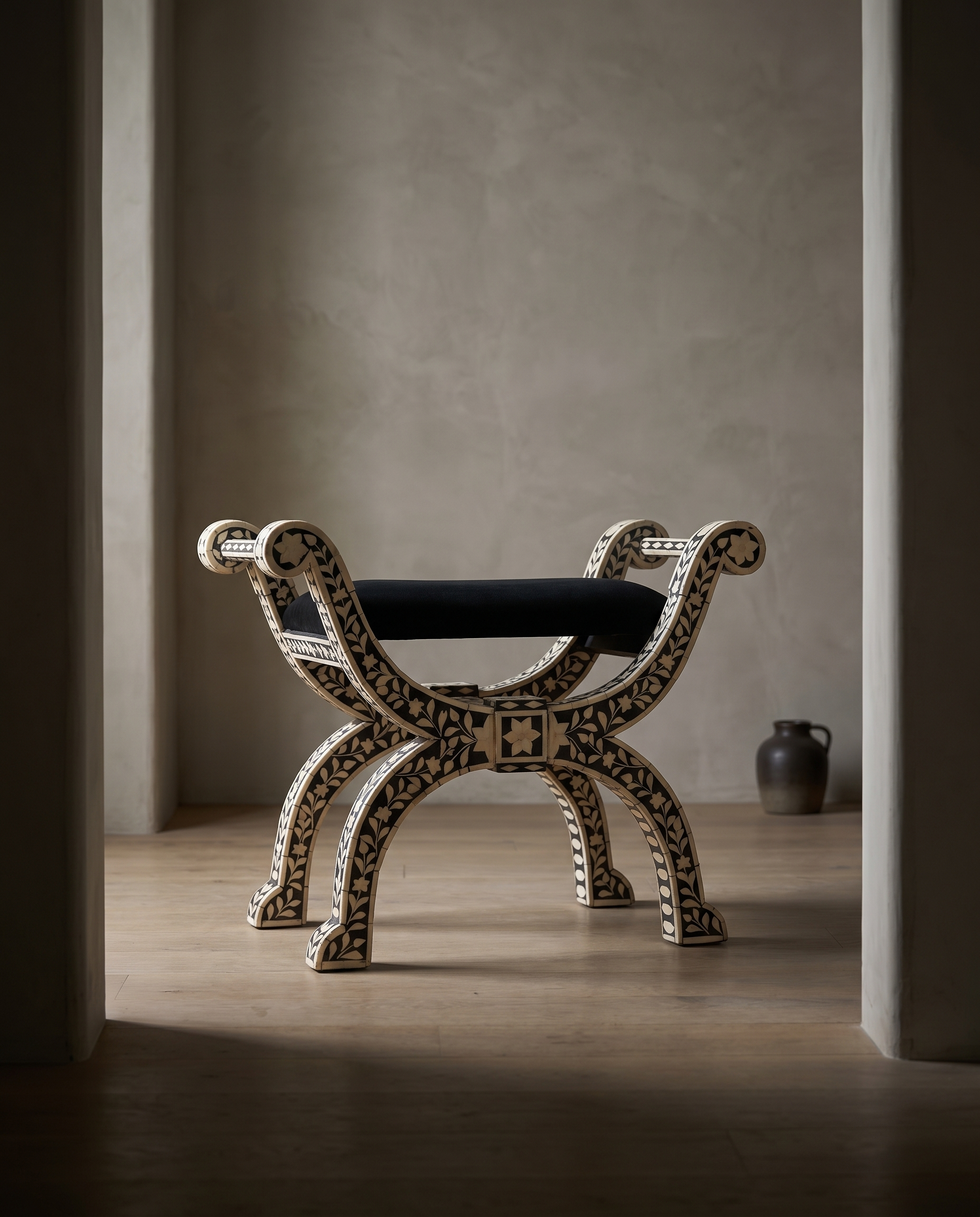 Bone inlay curule bench in a moody doorway vignette, greige plaster room