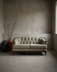 Sage diamond-tufted loveseat, front three-quarter hero view in a greige plaster room