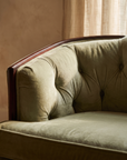 Detail of diamond button tufting and wood top rail on light sage velvet sofa