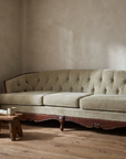 Light sage velvet tufted sofa, lifestyle view in a reading nook with a plant and low stool