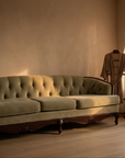 Light sage velvet tufted sofa, vintage French Provincial style, in a warm quiet corner with a robe hung by the window