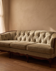 Light sage velvet tufted sofa, 45 degree three-quarter view showing full length and construction in warm low light