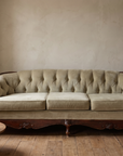 Light sage velvet tufted sofa, straight-on front-facing view in a lived-in room corner