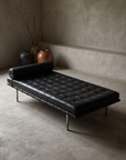 Mies van der Rohe Barcelona Daybed in black leather, staged in a greige plaster room with stoneware vessels and dried branches