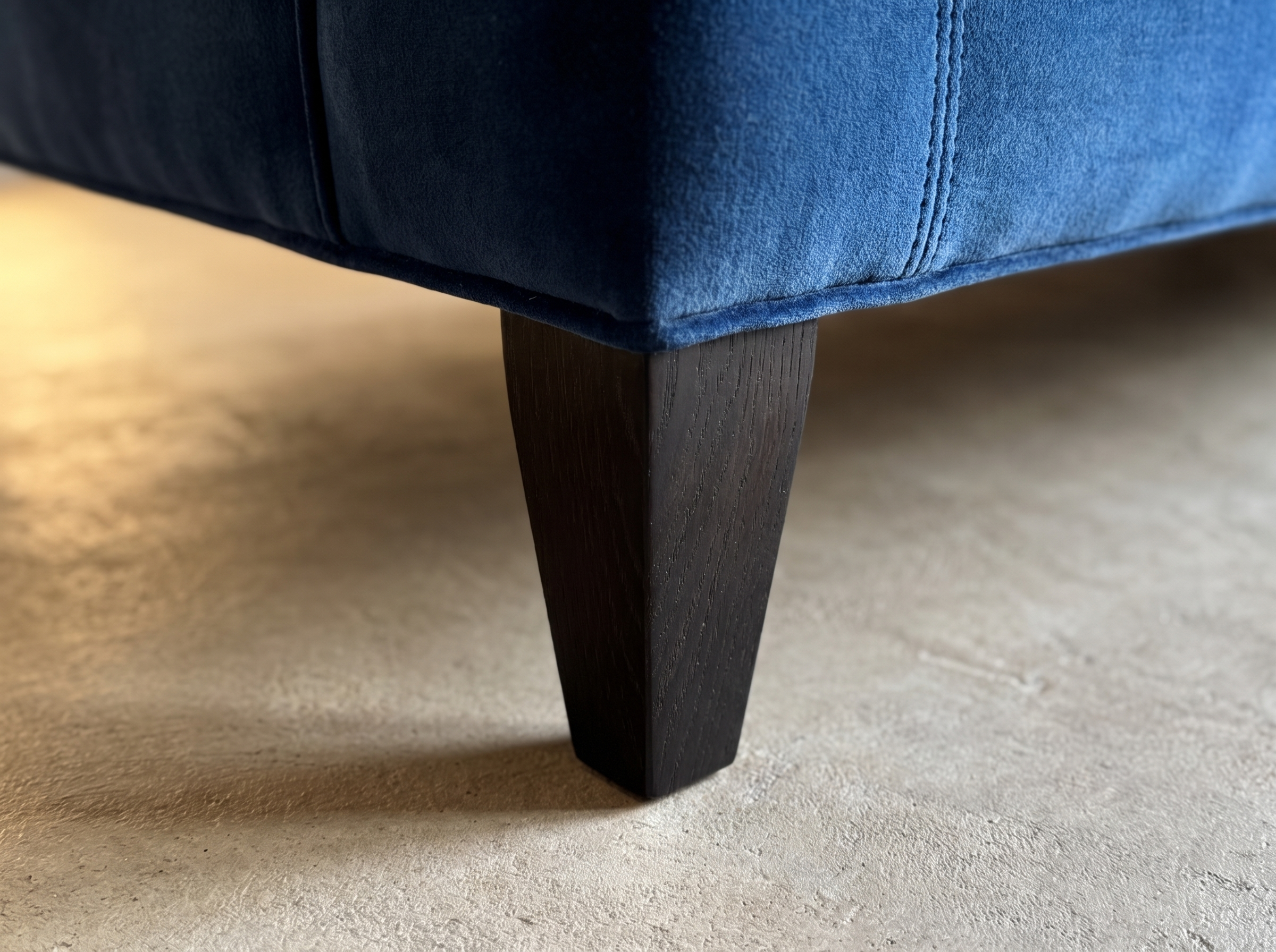 Macro detail of the tapered espresso wood leg and welted seam