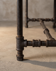 Close-up detail of the blackened iron pipe leg and H-stretcher joinery
