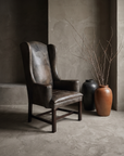 Brown leather RH wingback chair, three-quarter view, moodier light showing leather texture and scuffing