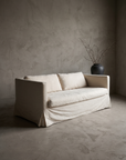 Three-quarter view of the linen track-arm sofa alone in a greige plaster room