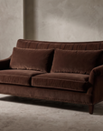 Taylor King espresso brown velvet English roll-arm sofa, lifestyle hero shot in a greige plaster room