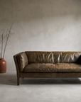 Cognac leather Groucho two-seater sofa, real worn patina with heavy creasing and a slouched seat, three-quarter lifestyle view in a greige plaster room with stoneware vessels