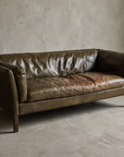 Cognac leather Groucho two-seater sofa, 45 degree three-quarter view showing the low tuxedo form and leather-wrapped legs