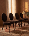 Four Mitchell Gold + Bob Williams oval-back dining chairs in espresso brown velvet, staged together in a warm candlelit dining room