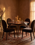 All four chairs pulled up around a round dining table set with candles in a warm, lived-in dining room