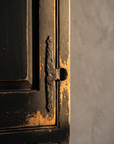 Detail of the Little Pantry Armoire's wrought iron strap hinge and thumb latch against the distressed black paint