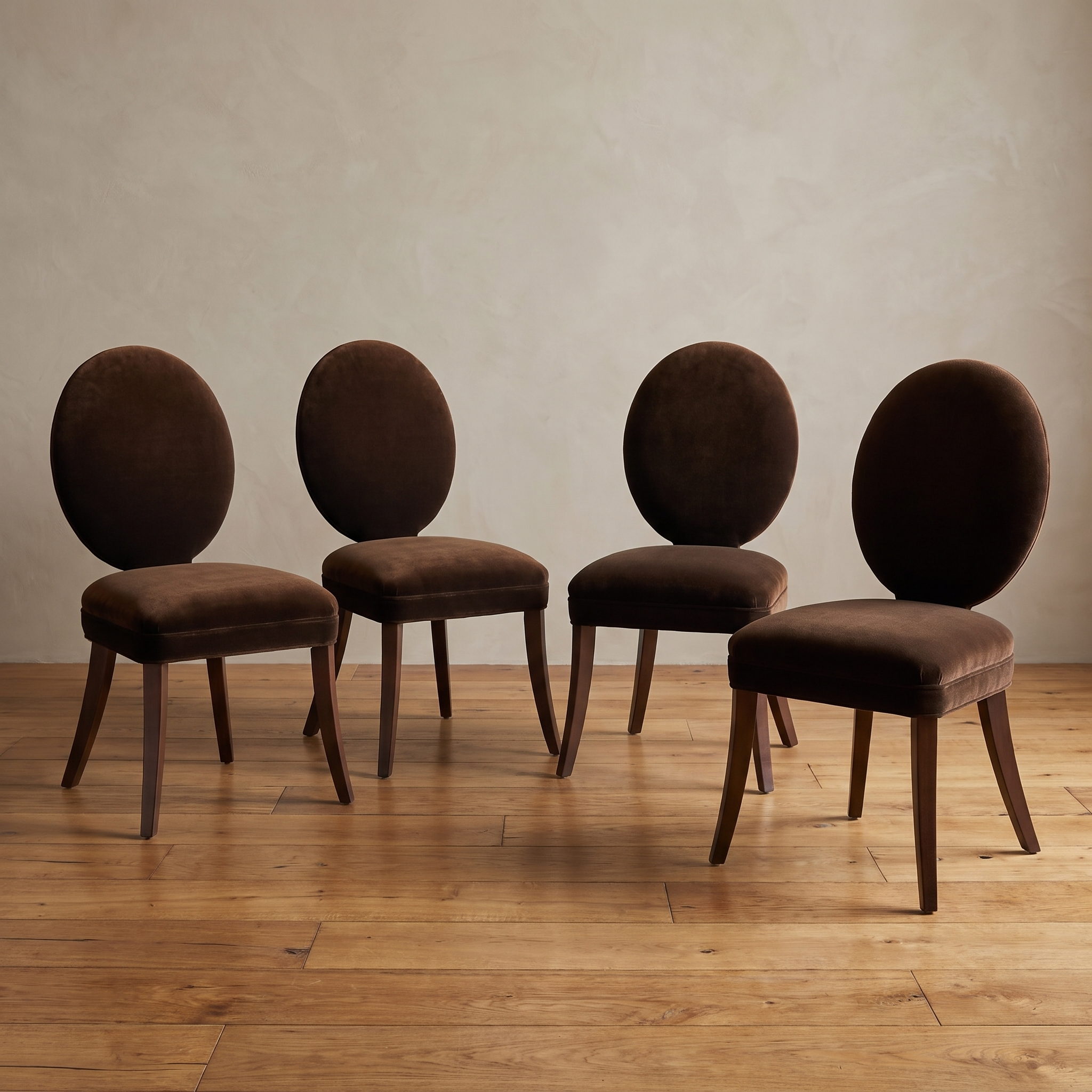 Four Mitchell Gold + Bob Williams oval-back dining chairs in espresso brown velvet, staged together against a plaster wall