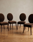 Four Mitchell Gold + Bob Williams oval-back dining chairs in espresso brown velvet, staged together against a plaster wall