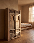 The Ubud Armoire styled in a warm, sunlit bedroom corner beside sheer curtains and a linen-dressed bed