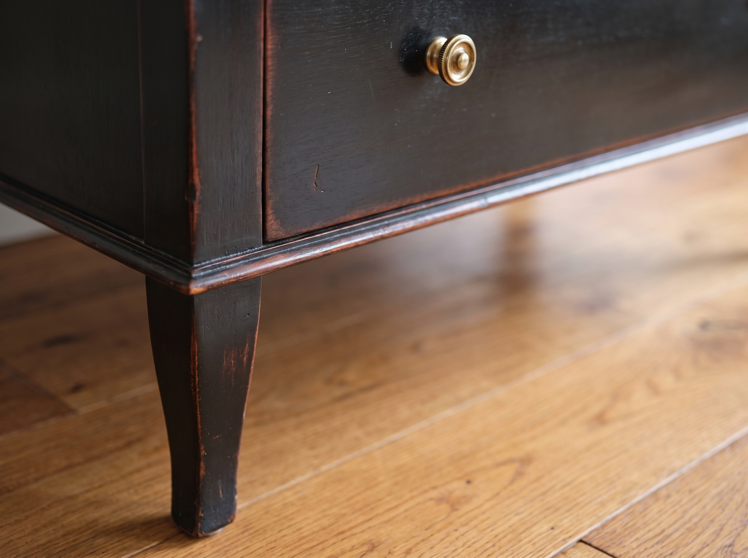 Detail of the tapered leg, worn ebonized finish, and brass ring pull