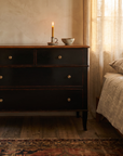 Atelier de Madeleine chest three-quarter view in a warm bedroom setting with a lit candle, kilim rug, Axel Vervoordt wabi-sabi style