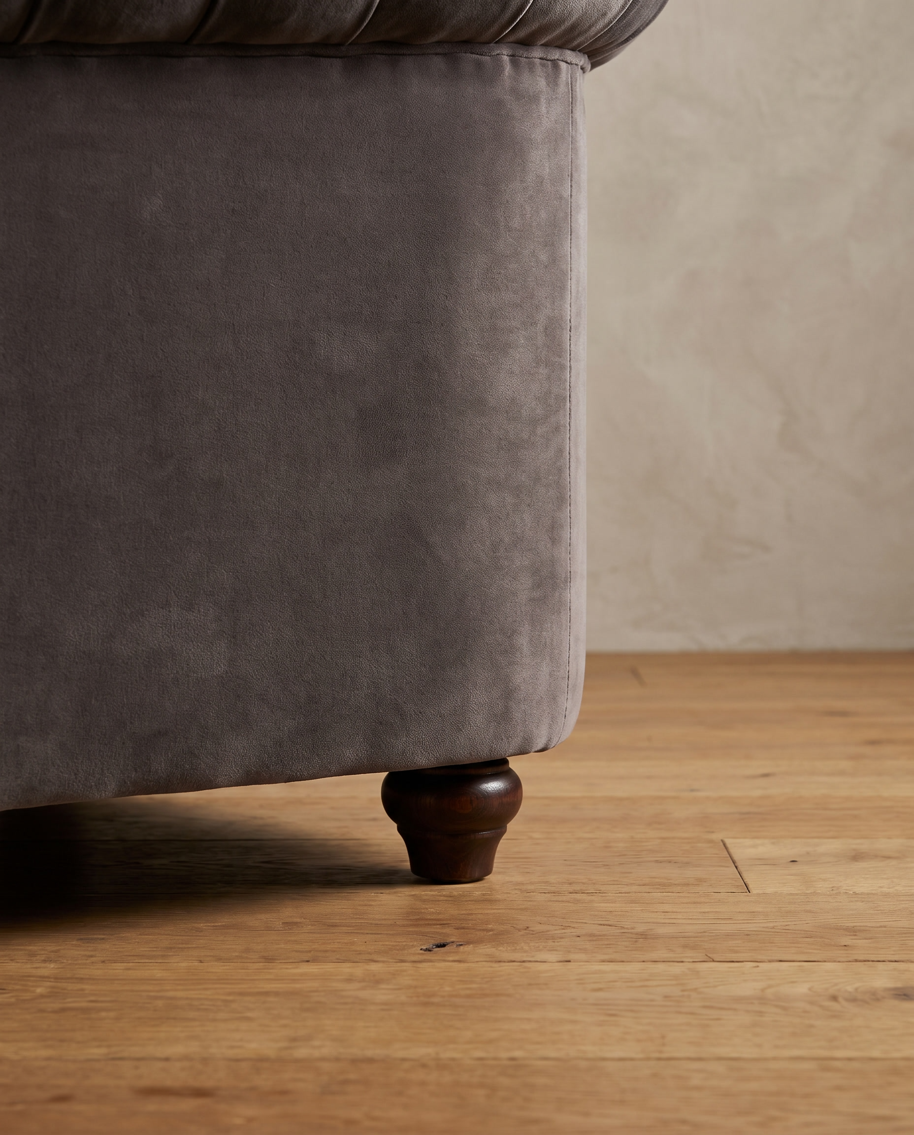 Macro detail of the turned dark wood bun foot on the smoke grey velvet barrel chair