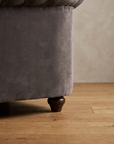 Macro detail of the turned dark wood bun foot on the smoke grey velvet barrel chair