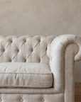 Detail of the rolled scroll arm meeting the button-tufted back, with the linen weave visible
