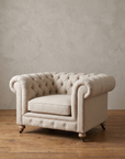 Natural linen tufted chesterfield chair-and-a-half, three-quarter view, against a troweled plaster wall on a reclaimed wood floor