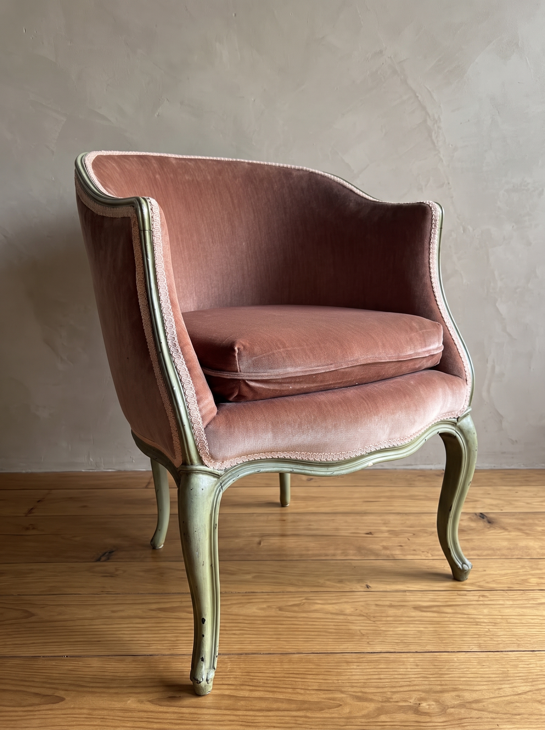 Front angle of the rose velvet bergère with cabriole legs on a reclaimed wood floor