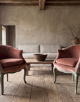 Pair of rose velvet bergères en gondole with sage green frames in a wabi-sabi living room with lime plaster walls, timber beams, a linen sofa and reclaimed oak floors