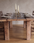 End view of the redwood dining table set with place settings, candlesticks and rush-seat chairs