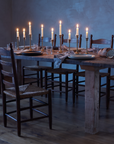 Redwood dining table after dinner at dusk with candles burned low, torn bread and chairs pushed back