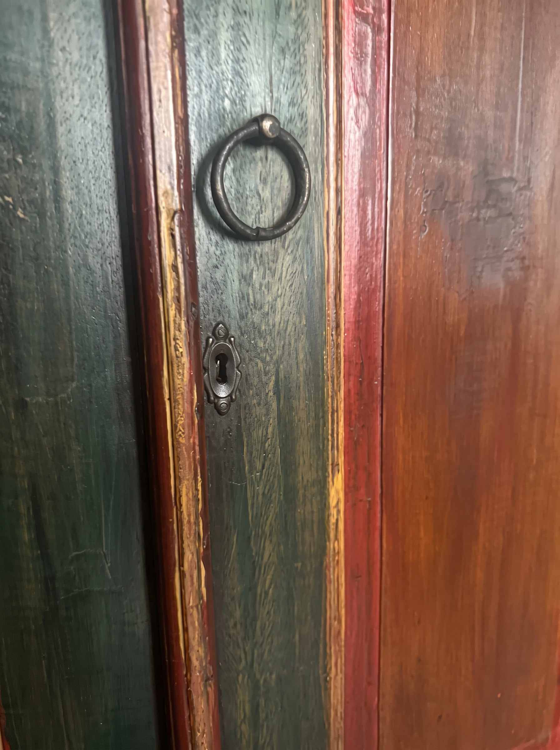 Macro of the iron ring pull and keyhole escutcheon on the armoire's distressed green-black door with red pinstripe