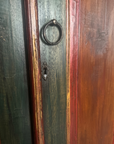 Macro of the iron ring pull and keyhole escutcheon on the armoire's distressed green-black door with red pinstripe