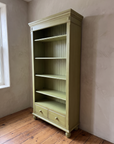 Three-quarter view of the olive green bookcase showing its plain side panel, drawers and reeded bun feet