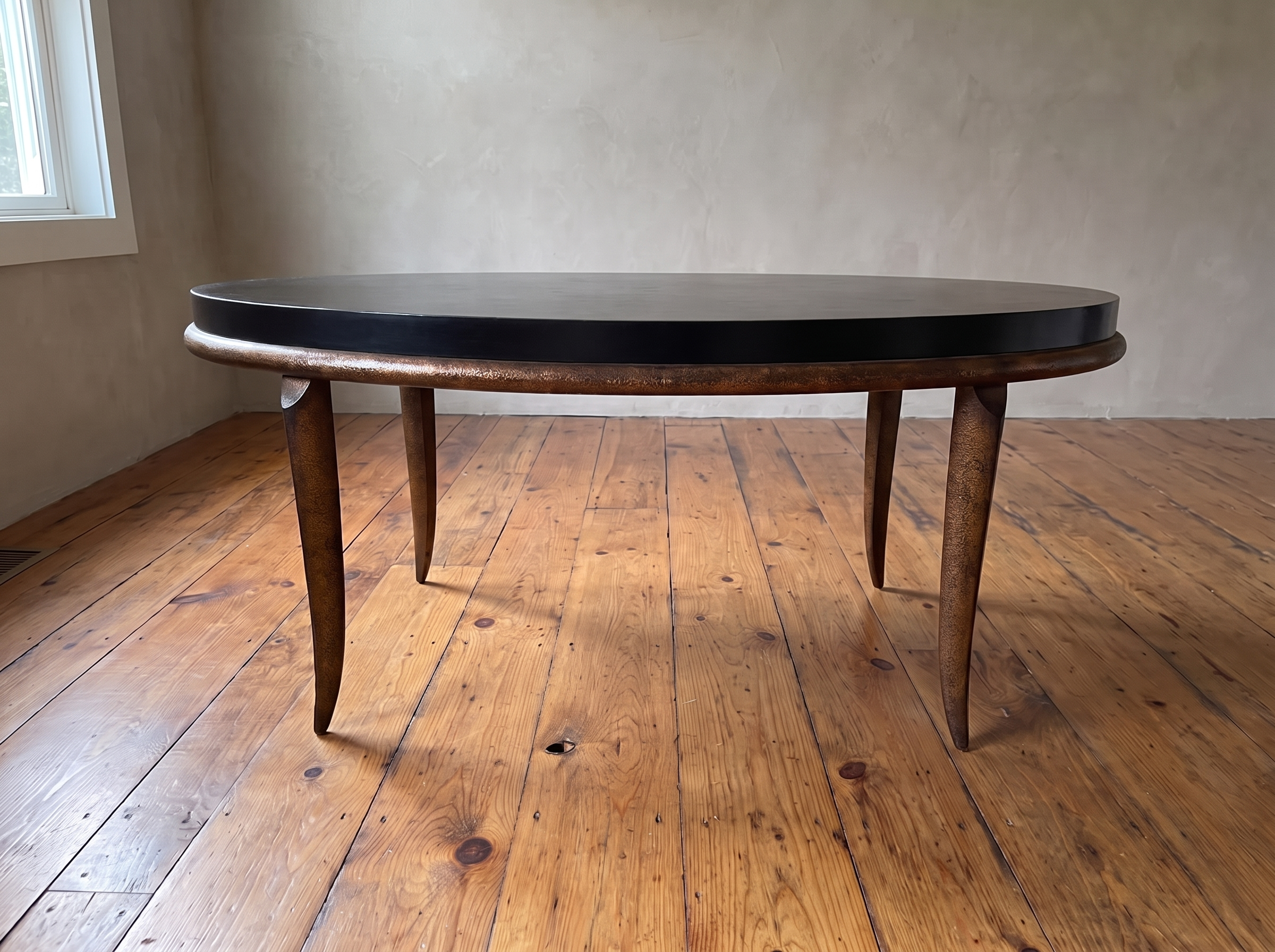 Side profile of the black and bronze oval coffee table showing four tapered saber legs, window light