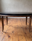 Side profile of the black and bronze oval coffee table showing four tapered saber legs, window light
