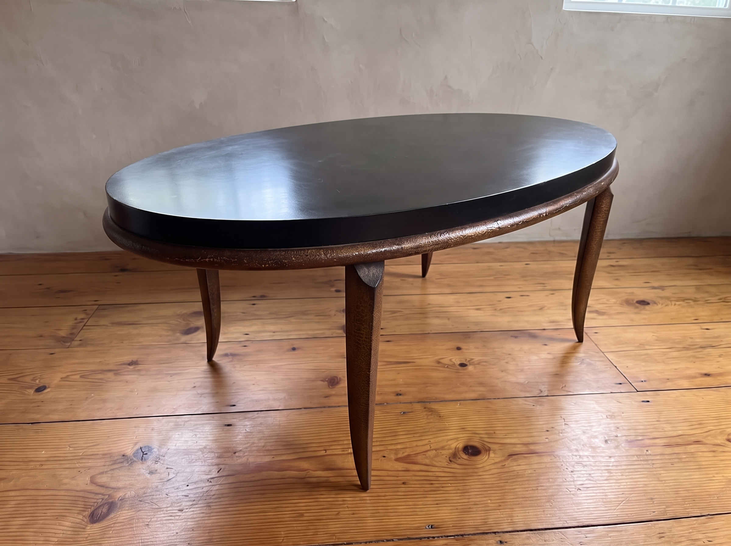 Black oval coffee table top with textured bronze rim, soft daylight on a reclaimed wood floor