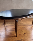 Black oval coffee table top with textured bronze rim, soft daylight on a reclaimed wood floor