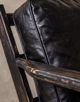 Close-up of the distressed black oak paddle arm against the black leather back cushion