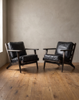 A pair of black leather lounge chairs with black distressed oak frames angled toward each other against a warm plaster wall on a reclaimed wood floor