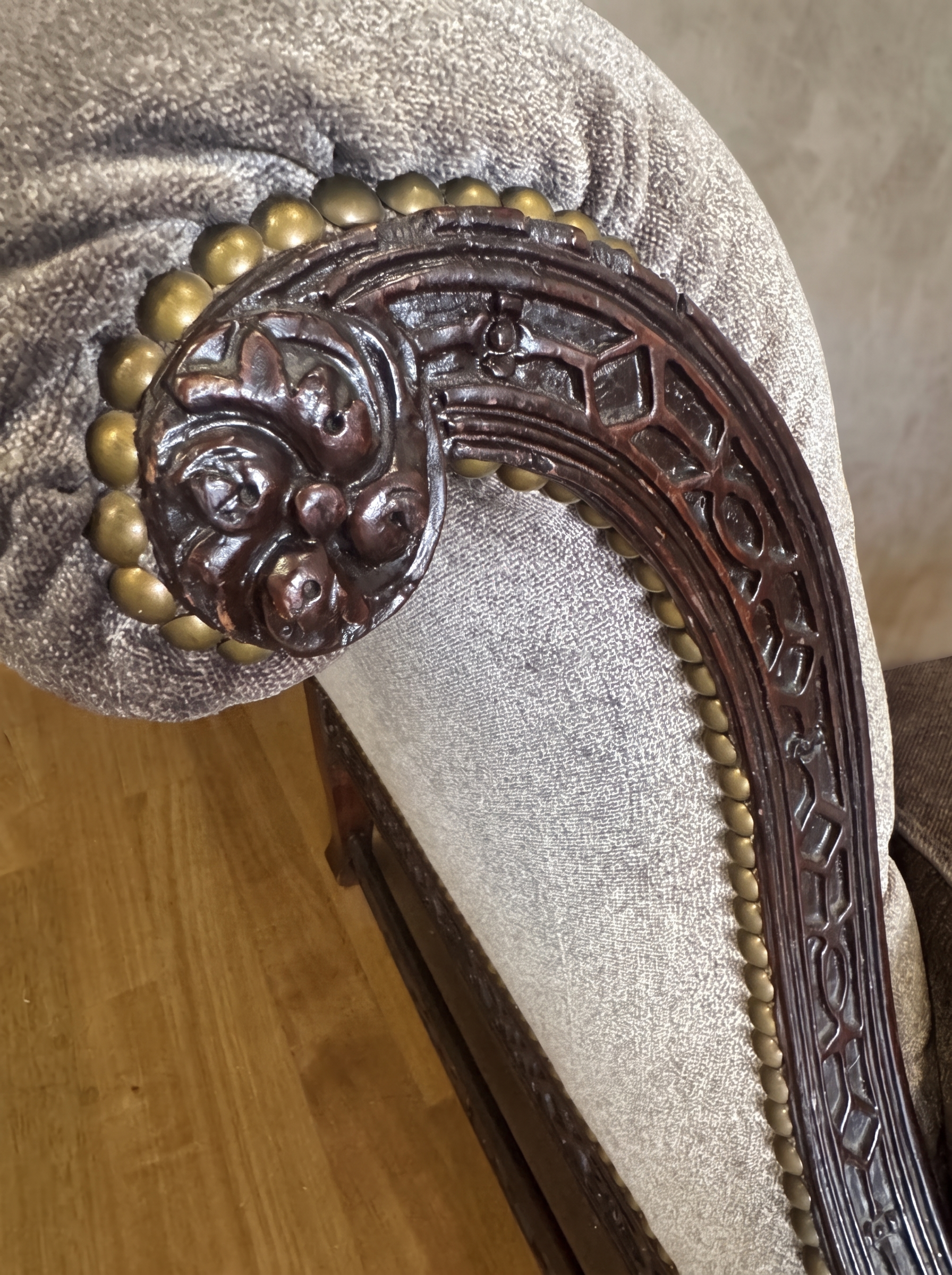 Close-up of the hand-carved leafy arm end ringed in large brass nailheads, with lattice fretwork facing