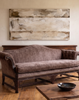 Mauve velvet camelback sofa floating in a calm limewash living room, antique console behind it, a large bone-and-umber abstract painting above, live-edge walnut coffee table in front